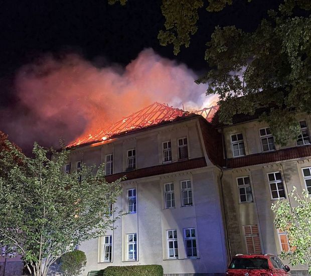 Aus einem Dach eines Mehrfamilienhauses lodern Flammen