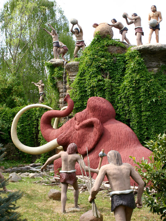 Saurierpark Kleinwelka nachgestellte Szene (aus Kunstmaterialien)- ein Mammut ist in die Falle der Steinzeitmenschen gegangen, die Menschen kommen sofort und töten es, von einer Klippe aus schieben und werfen andere Felsen hinunter