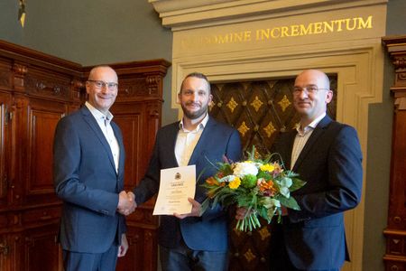 Karsten Vogt und Dr. Robert Böhmer gratulieren Heiko Nowak, er bekommt eine Urkunde und einen Blumenstrauß