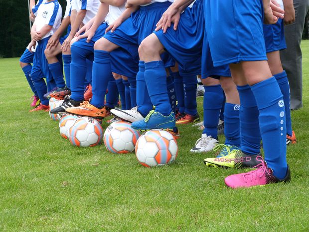 Fußballer stehen mit einem Fuß auf Ball, alle tragen blaue Socken und Hosen
