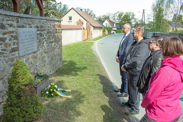 Oberbürgermeister Karsten Vogt und 3 Ortschaftsräte stehen vor der Gedenktafel und dem niedergelegten Kranz am Ort der ehemaligen Scheune; auf der Tafel steht: Zum Gedenken an 195 Opfer die in dieser ehemaligen Scheune, am 22. April 1945 von Angehörigen der 1. Ukrainischen Front, verbrannt wurden.