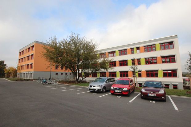 Curie Grundschule Curie Schule- weiß-orangnes Gebäude mit einzelnen grünen oder orangenen Streifen unter den Fensterbrettern