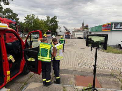 Zwei Feuerwehrleute neben einem Einsatzfahrzeug auf den Parkplatz im Hintergrund Rauch vom Brand des Batteriespeichers