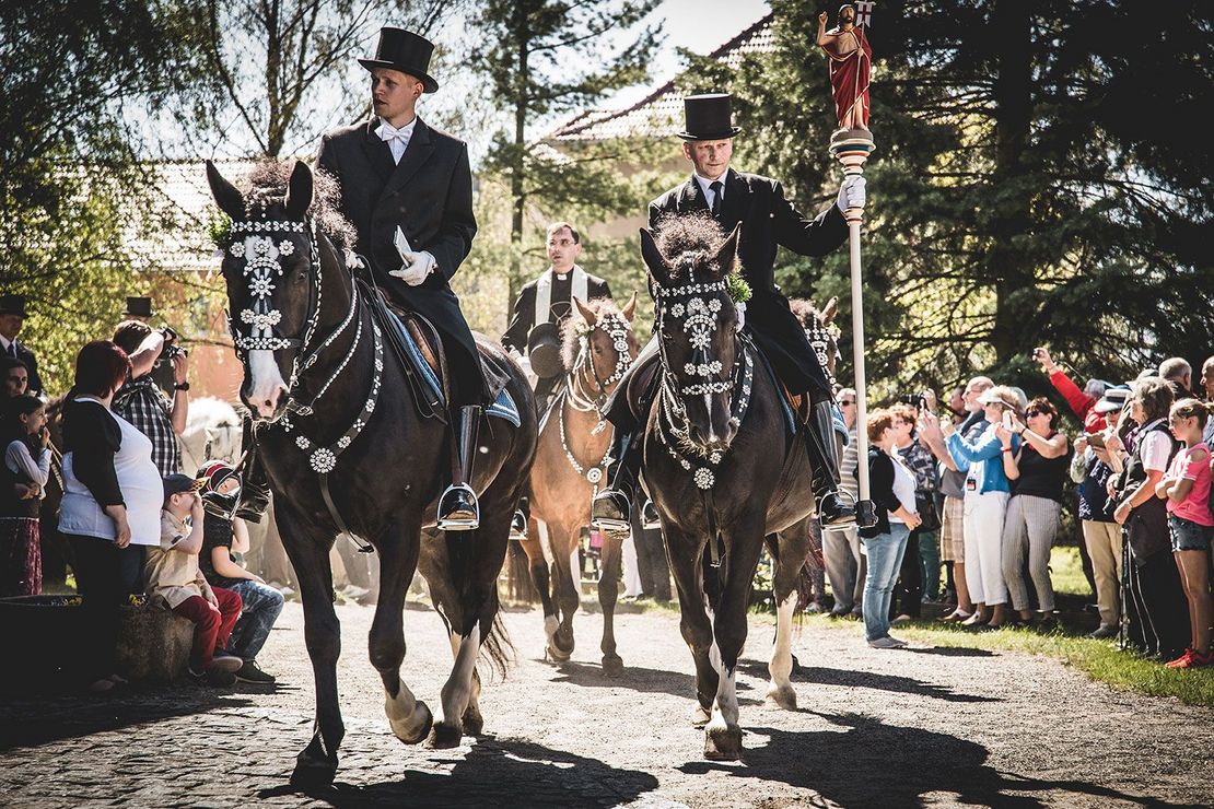 Osterreiter reiten einen Weg entlang links und rechts schauen Menschen zu.