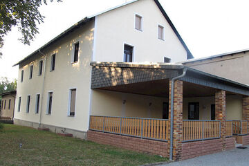 großes weißes Haus mit Spitzdach und überdachter Terrasse