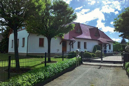 Hofzufahrt gesäumt von Bäumen und Sträuchern, großes weißes Haus mit rotem Dach