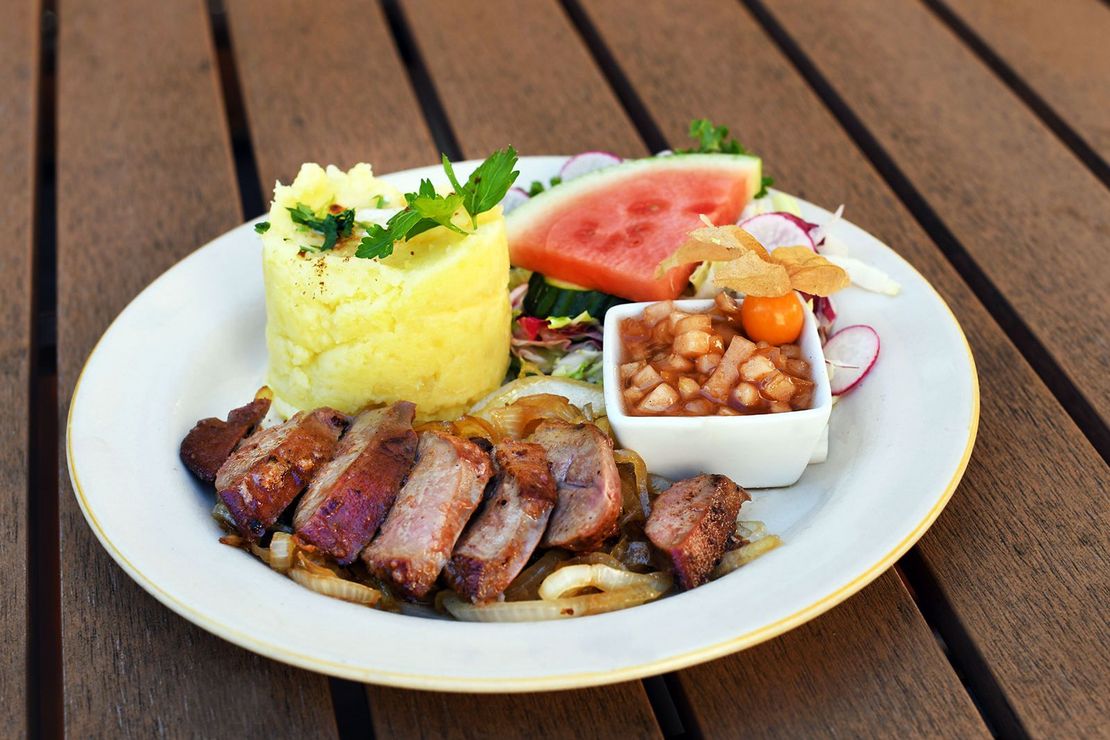 Teller angerichtet mit Leber und Kartoffelpüree, dekoriert mit roter Melonenscheibe und grüner Petersilie