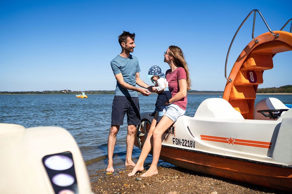 Vordergrund junge Familie mit Kind an Tretboot, Hintergrund Stausee