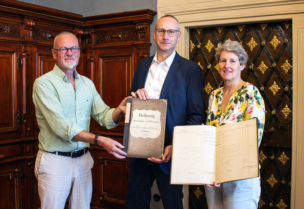 Zwei Männer und eine Frau halten zwei historische Bücher in der Hand