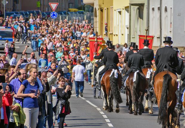 Männer in schwarzen Anzügen reiten auf Pferden und viele Menschen schauen zu.