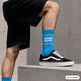 Mann mit kurzen schwarzen Hosen hat reichten Fuß auf eine flache Mauer gestellt. Er trägt schwarze Sportschuhe mit weißer Sohle. Und türkisfarbene Socken mit weißer Schrift am Schaft Ohne Senf