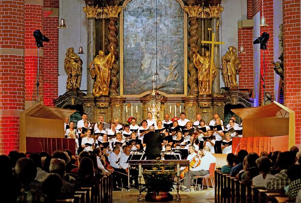 Frauen und Männer in weißen Blusen und Hemden stehen vor einem Altar und singen 