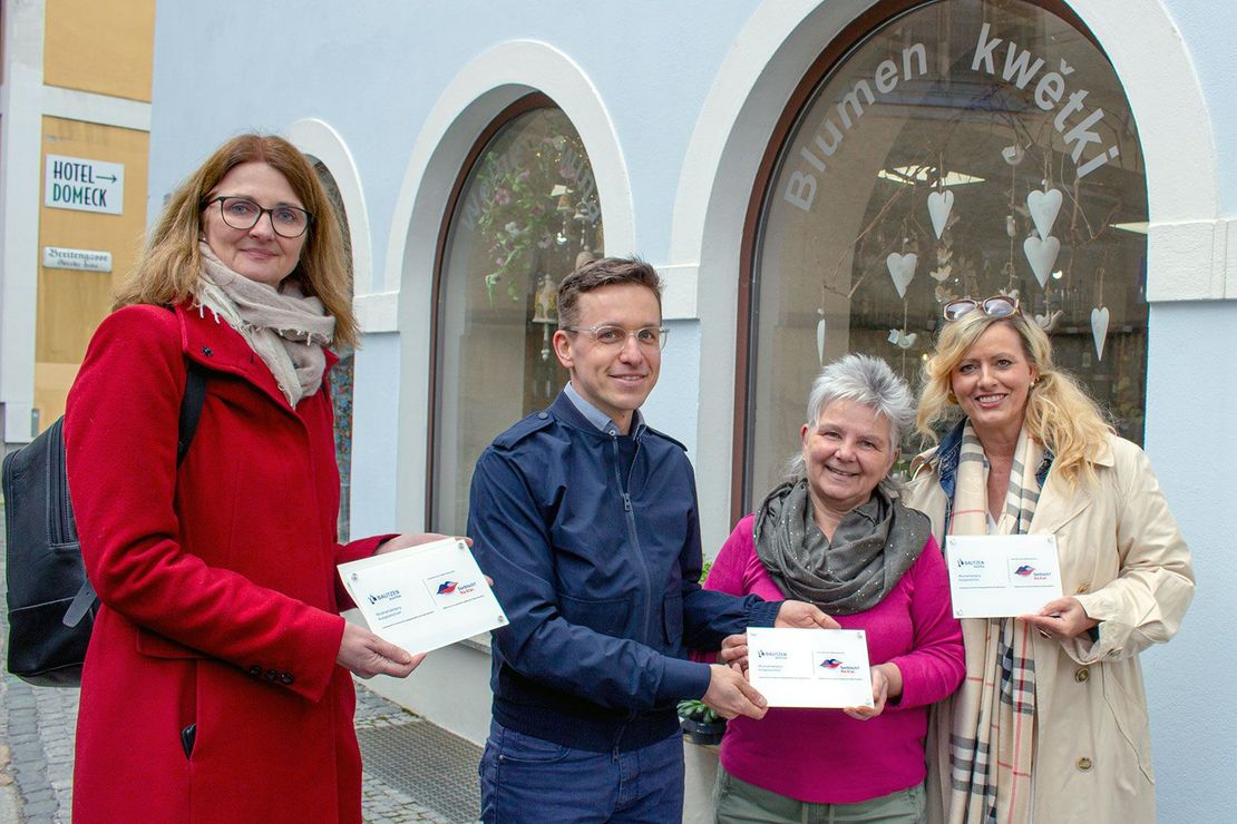 Drei Frauen und ein Mann stehen vor dem Geschäft Moosmutzel und halten eine Plakette in der Hand