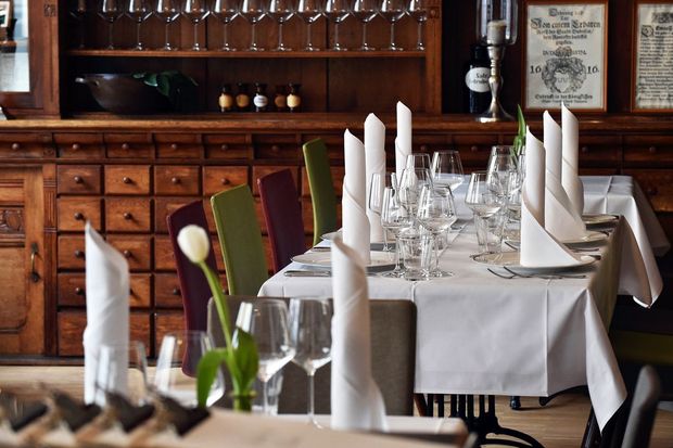 Tische mit weißer Tischdecke und rot oder grünen Stühlen, auf den Tischen stehen Gläser und Teller mit gerollten Servierten