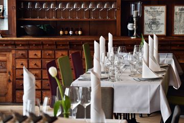 Tische mit weißer Tischdecke und rot oder grünen Stühlen, auf den Tischen stehen Gläser und Teller mit gerollten Servierten