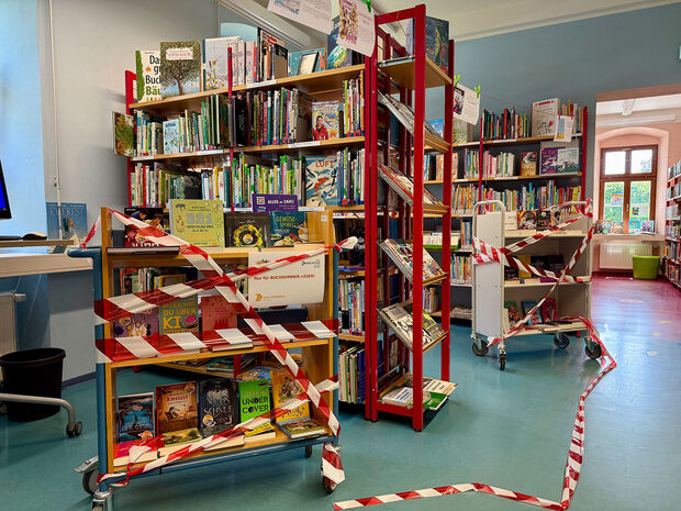 Bücherregal mit neuen Büchern und durchgeschnittenem Absperrband darum