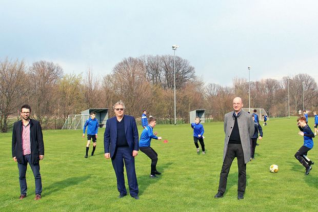 3 ältere Herren stehen vor einem Jugendfußballspiel