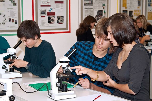 Drei Schüler führen ein biologisches Experiment, mit Mikroskop durch