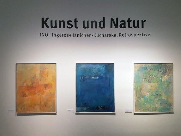 Wand im ersten Raum der Sonderausstellung " Ino - Kunst und Natur". Zu sehen sind drei Gemälde Inos in leuchtenden Farbe. Darüber der Titel der Ausstellung.