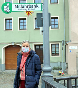 Mitfahrbank im Stadtteil Seidau Frau steht unter einem grünen Schild
