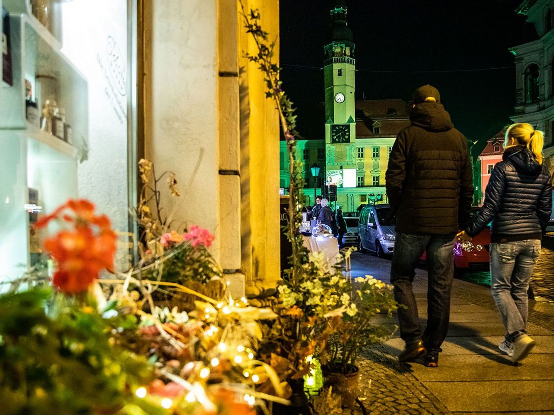 Junges Paar läuft Hand in Hand im abendlichen Bautzen auf das auf das Rathaus zu (gelb). Im Vordergrund ein dekoriertes Schaufenster.