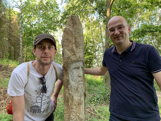 Zwei Männer stehen neben einen steinernen Kunstwerk
