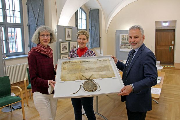 Zwei Frauen und ein Mann präsentieren eine restaurierte historische Urkunde