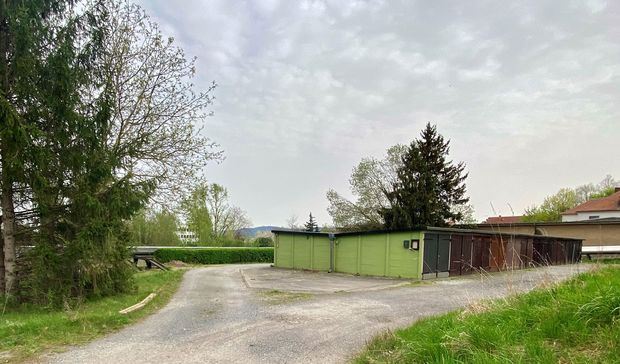 Garagenkomplex in grün/braun im Mittelgrund, grüne Bäume drumherum