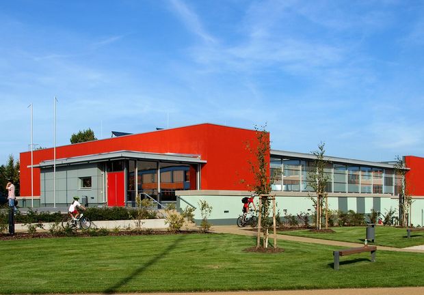 Mehrzweckhalle in den Farben rot und graugrün, davor eine grüne Wiese 