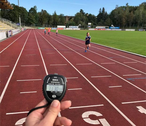 Kinder laufen auf Laufbahn und eine Stoppuhr zeigt die Zeit