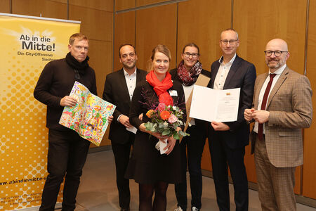 Preisverleihung Wettbewerb „Ab in die Mitte“ sechs Personen nehmen Urkunde und Blumen entgegen