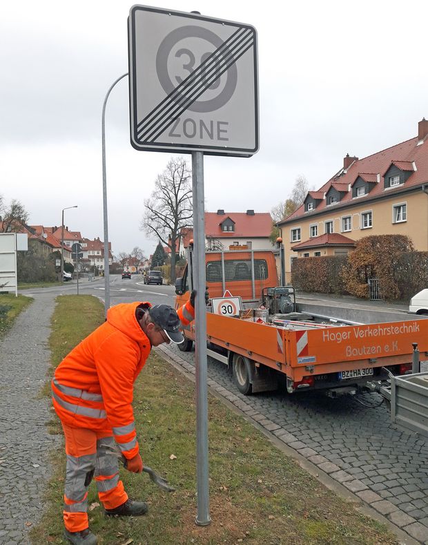 Mann in orangener Kleidung stellt ein Verkehrsschild auf