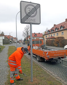 Tempo-30-Schild Mann in orangener Kleidung stellt ein Verkehrsschild auf