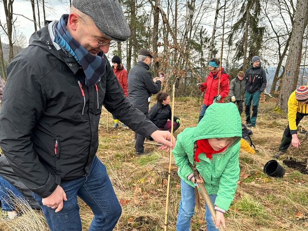 Tag des Bautzener Stadtwaldes 2024 Mann hält den zu pflanzenden Baum fest. Mädchen füllt das Pflanzloch mit Erde auf.