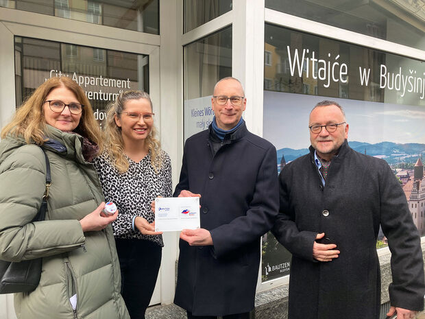 Sorbische Beschriftungen Zwei Frauen und zwei Männer stehen vor einem Schaufenster und halten ein kleines Schild in der Hand