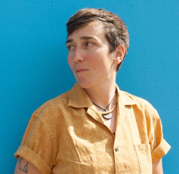 Die Autorin steht vor einer blauen Wand, den Kopf zur Seite gerichtet.