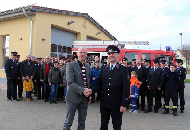 Übergabe Feuerwache Niederkaina Feuerwehrleute in Uniform vor Feuerwehrauto und vor gelben Gebäude