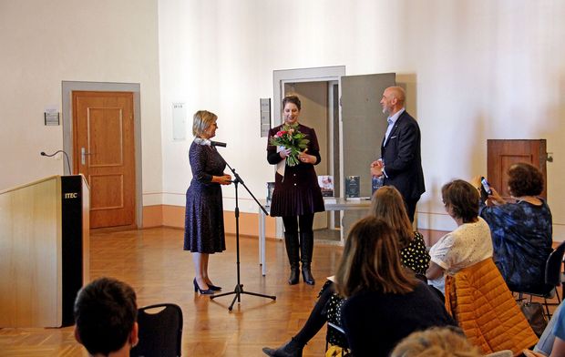 Buchsommer Sachsen Der Bürgermeister steht mit zwei Frauen vor einem Publikum. Eine der Frauen bekommt einen Blumenstrauß geschenkt