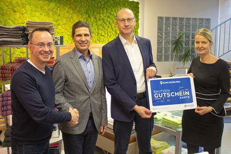 4 Personen stehen in einer Reihe, 2 Männer geben sich die Hand und eine Frau und ein Mann halten den City Gutschein 