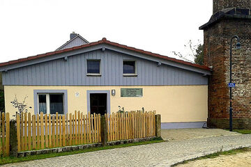 Ferienwohnung „Alte Brennerei“ gelbes Haus mit Spitzdach, oben graue Holzverkleidung