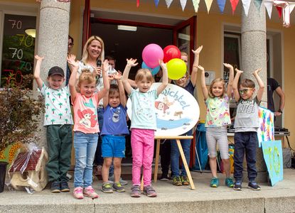 Spreewichtel Kinder stehen, lachend ihre Hände in die Luft werfend, vor der Kita Spreewichtel