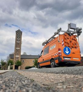 Messfahrzeug Orangefarbenes Messfahrzeug fährt auf einer Straße. Im Hintergrund ist ein Turm zu sehen.