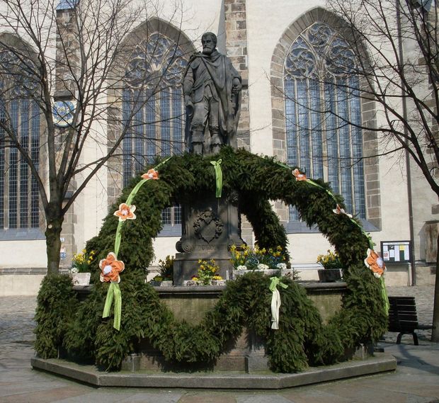 Osterbrunnen vorm Dom mit Tannengrün, Narzissen und kleinen Blumengirlanden geschmückt