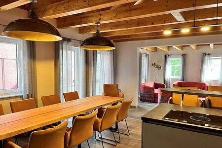 vorn großer Esstisch und Küchenblock, hinten Wohnbereich mit Sofas, sichtbare Deckenbalken