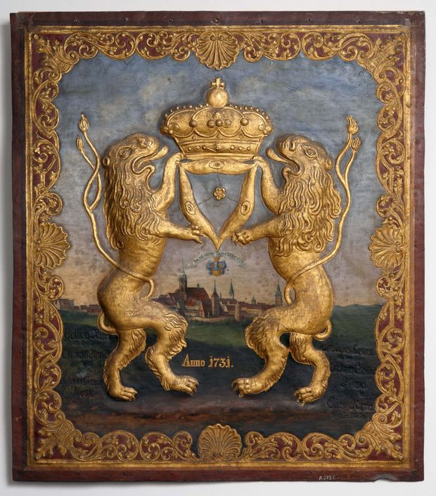 Ein rechteckiges Schild aus Metall. darauf wurde die Ansicht der Satdt Bautezn aus der ferne gemalt. Im Vordergrund stehen als Relief aufrecht zwei goldene Löwen, die in ihren Vorderpfoten eine goldene Krone über die Stadt halten. Es ist das Wappen der Tuchmacher aus 1731.