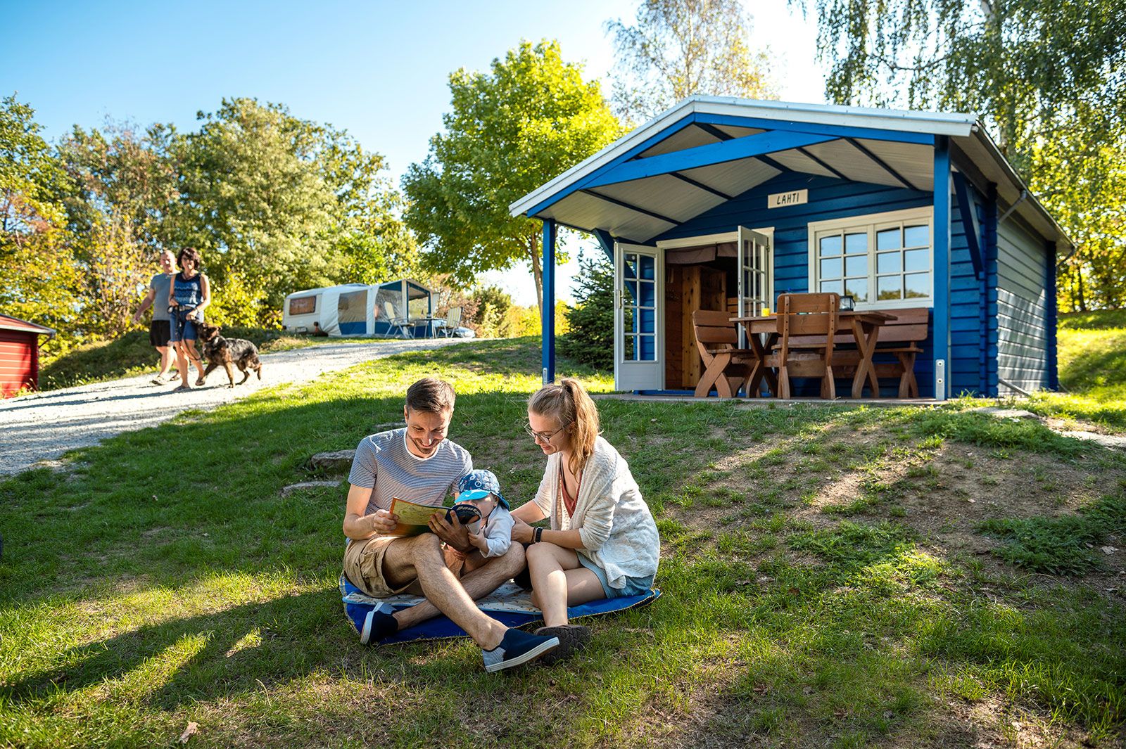 Stausee Campingplatz eine Familie sitzt vor einer Holzhütte auf der Wiese