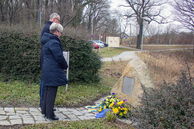 Gedenken Groß Rosen Frau in blauer Jacke und Mann in schwarzem Mantel stehen vor einen Gedenkstein. Davor liegen Blumengebinde.