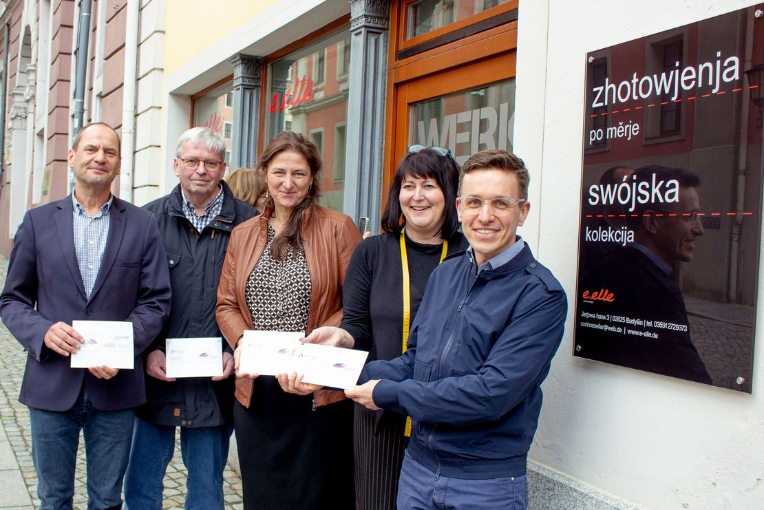 Zwei Frauen und drei Männer mit Schildern in der Hand stehen vor dem Geschäft e.elle