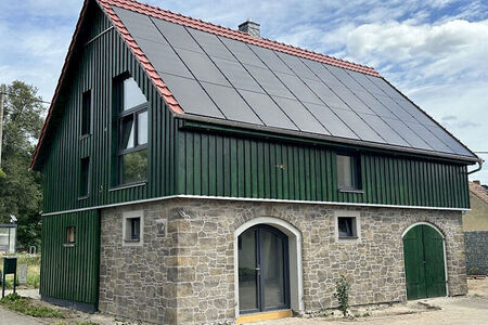 Haus mit Steinoptik im Untergeschoss und grüner Holzverkleidung im Obergeschoss, rotes Spitzdach mit Soloaranlage