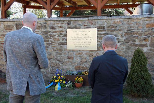 Zwei Männer stehen in stillem Gedenken vor einer Gedenktafel 